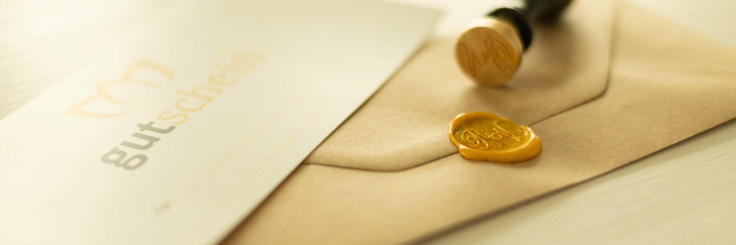 Braunes Kuvert mit gelbem Wachssiegel und Stempel daneben auf hellem Untergrund